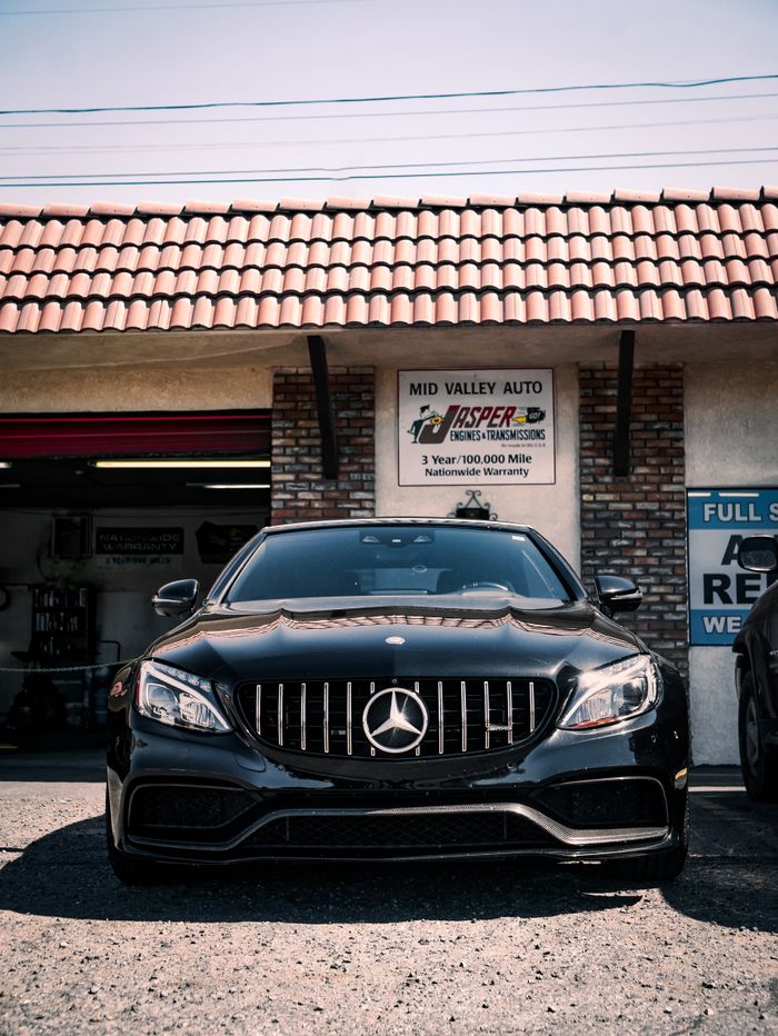 Front view of a black Mercedes-Benz sedan parked at a local auto shop on a sunny day.
