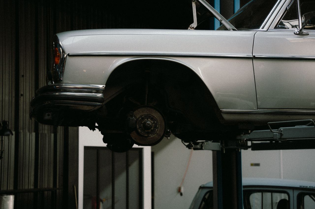 A classic car is elevated on a lift in a professional auto repair garage, showcasing its undercarriage.